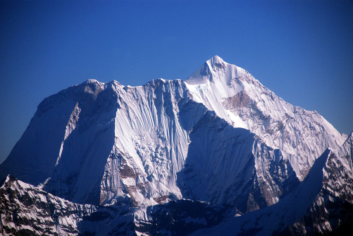 Kathmandu Mountain Flight 05-1 Menlungtse The dramatic south face of Menlungtse (7181m) shines in the early morning sun on the Kathmandu mountain flight. Menlungtse has a long summit ridge from the lower west summit (7023m) on the left to the higher east summit (7181m) on the right. Menlungtse has only been climbed a few times because of its extremely difficult steep faces. The Menlung La pass from Nepal into Tibet is on the lower right.